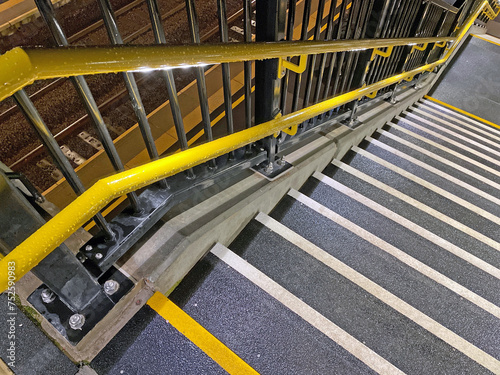 Bright yellow handrails and non-slip steps on staircase at railway station in UK.
