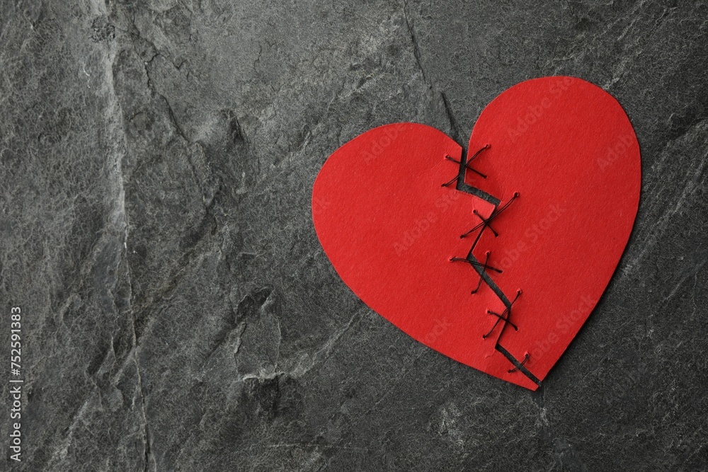 Broken heart. Torn red paper heart sewed with thread on dark grey table, top view. Space for text