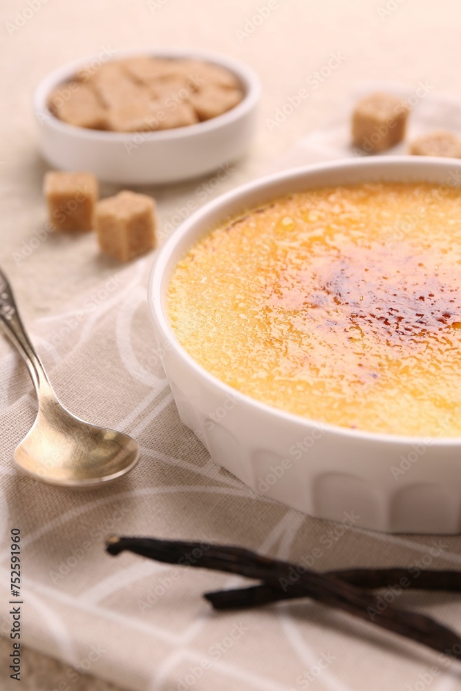 Delicious creme brulee in bowl, vanilla pods and spoon on table, closeup Delicious creme brulee in bowl, vanilla pods and spoon on table, closeup
