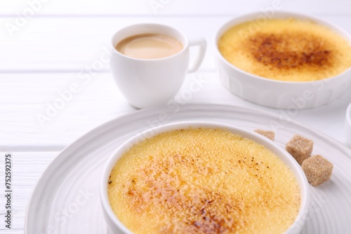 Delicious creme brulee in bowls, sugar cubes and coffee on white wooden table, closeup