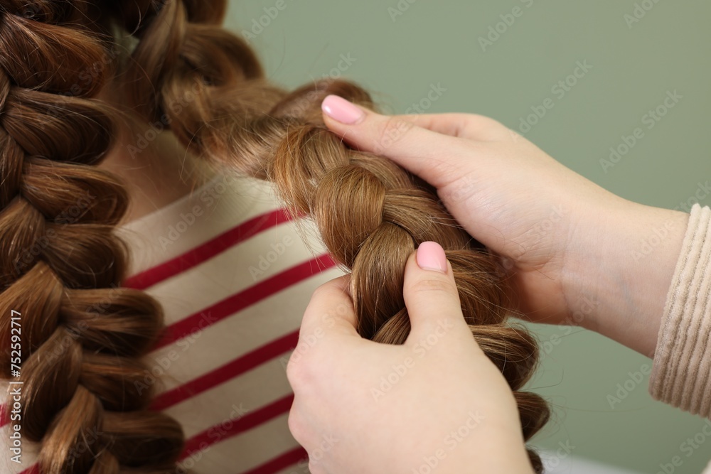 Naklejka premium Professional stylist braiding woman's hair on olive background, closeup