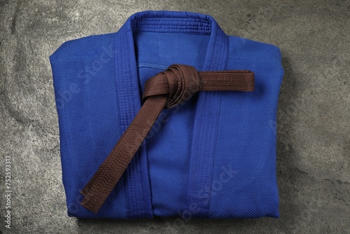 Brown karate belt and blue kimono on gray background, top view