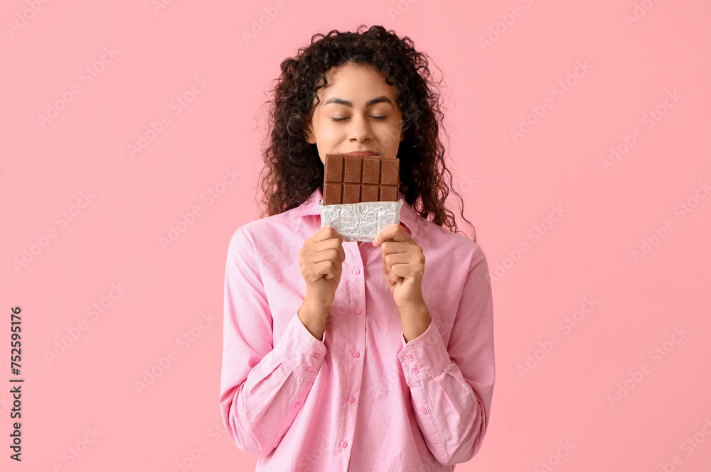 Beautiful young African-American woman with sweet chocolate bar on pink background Beautiful young African-American woman with sweet chocolate bar on pink background