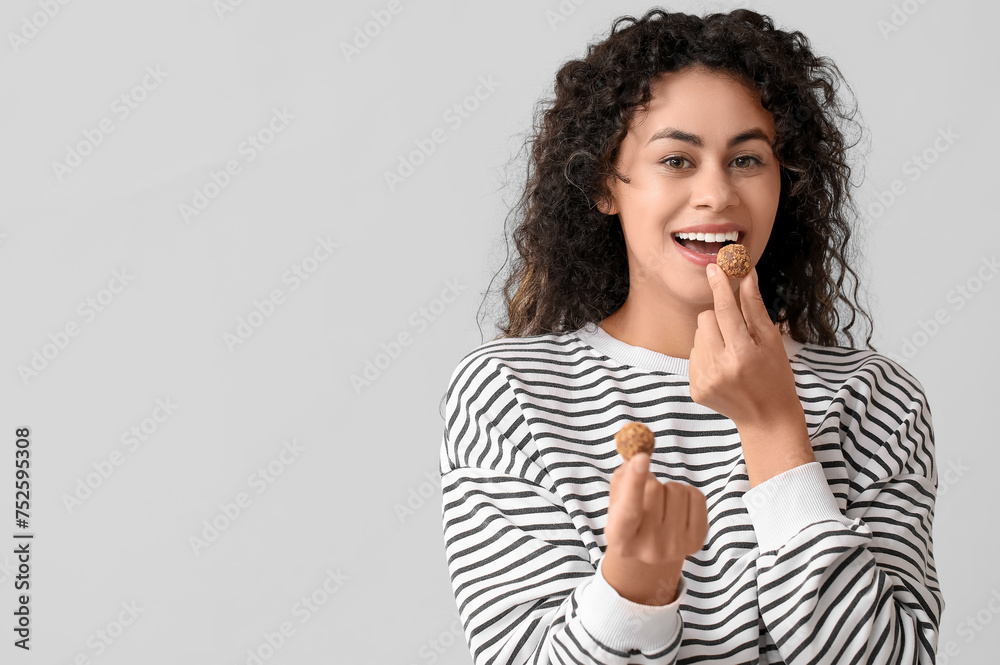 Beautiful young African-American woman with sweet chocolate candies on grey background Beautiful young African-American woman with sweet chocolate candies on grey background