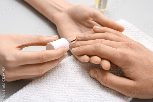 Manicure master applying cuticle oil onto male fingernails on grey background  closeup