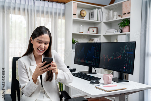 Smiling young Asian businesswoman with happy face looking on smartphone in profitable of exchange stock market graph at modern office. Concept of investing high profit in wealth security. Stratagem.