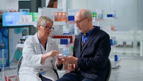 Proficient pharmacist in drugstore with patient, suggesting him heart arrhythmia medication pills to treat disease symptoms. Octogenarian man receiving treatment from employee
