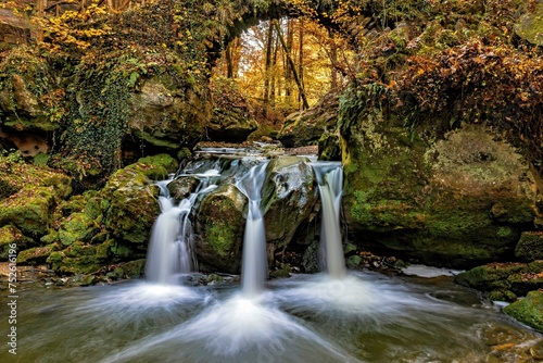 The three-armed Schiessentuempel waterfall in the Mullerthal in Luxembourg in sunny autumn weather as a long exposure photo