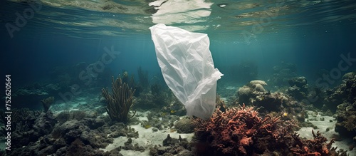 A white plastic bag floats on the surface of a coral reef, representing environmental pollution. The coral reef ecosystem is under threat as marine life may mistake the bag for food, leading to © AkuAku
