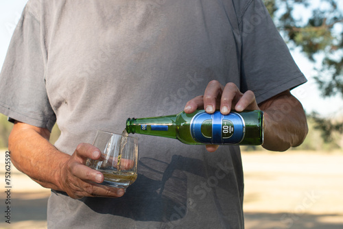 Man pouring a bottle of cold blue label  0.0 alcohol free beer into a glass on a hot sunny day, sun shadow on t-shirt