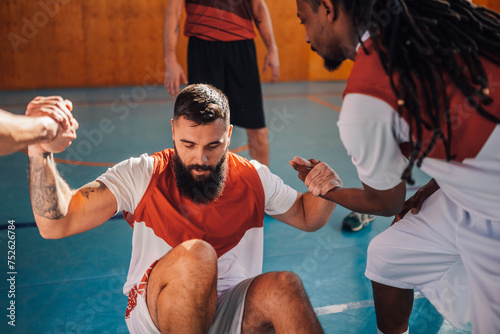 Basketball player trying to stand up with help of his interracial teammates.