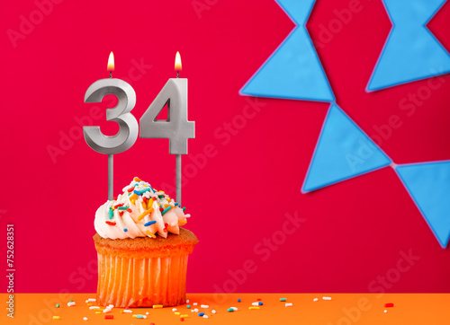 Number 34 candle with birthday cupcake on a red background with blue pennants