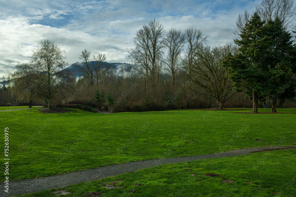 2024-02-20 CONFLUENCE PARK IN ISSAQUAH WITH LUSH GREEN GRASS AND TREES LINING THE SIDE WITH A MOUNTAIN AND BEAUTIFUL SKY IN THE BACKGROUND
