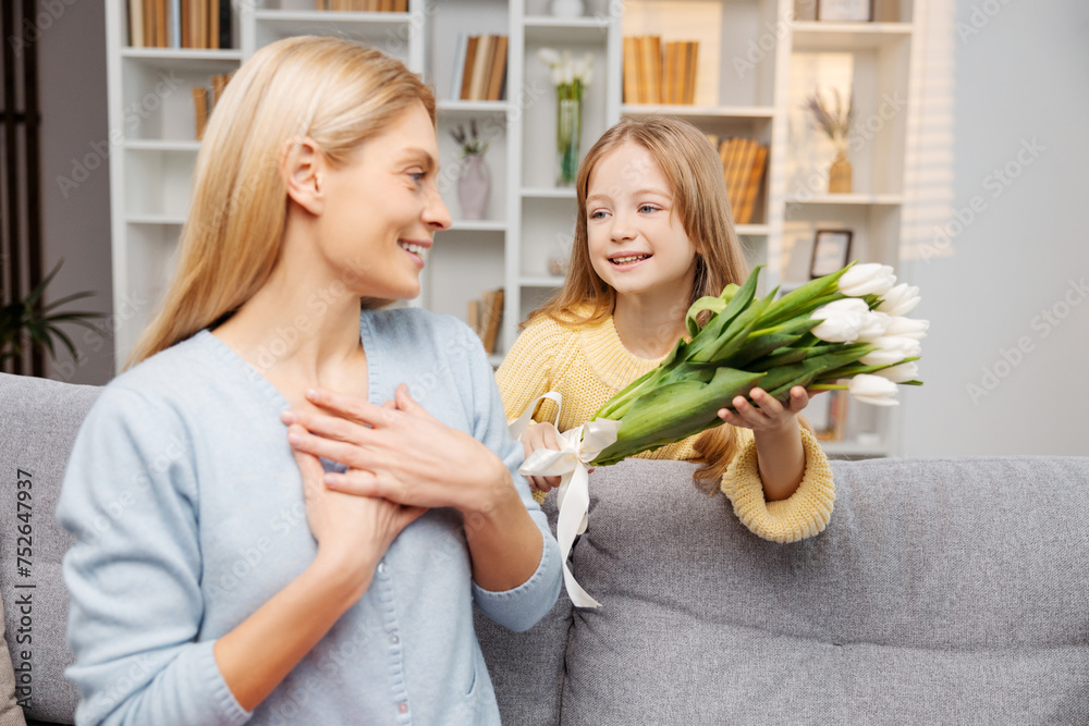 Happy family celebrating Mother's Day. Mother receiving tulips, surprised by her smiling daughter