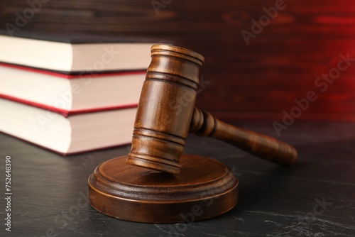 Wooden gavel and stack of books on dark textured table, closeup