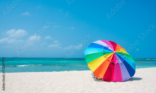 Multicolour vibrant rainbow beach umbrella on a beautiful hot and clear sunny day, with cruise ship on the horizon, turquoise water, Arashi Beach, Aruba, Caribbean Sea. Photo taken in February 2024. photo