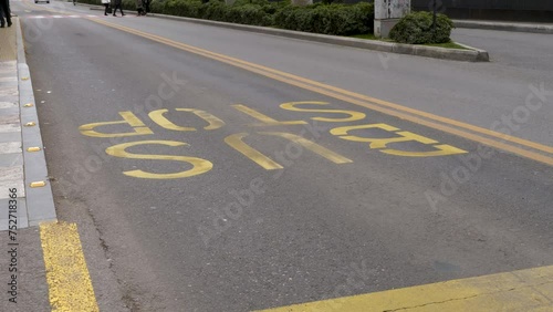 Pedestrians crossing bus lane with BUS STOP sign printed on an asphalted road with yellow paint. photo