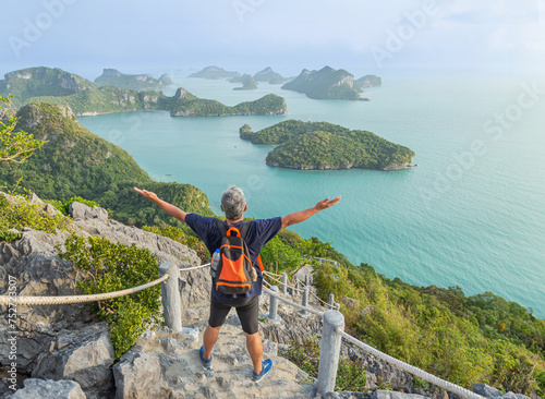 The man with backpack  raised up arms celebrate standing on high cliff Pha Jun Jaras view point the peak of mountain at Wua Ta Lap island Surat Thani, Thailand