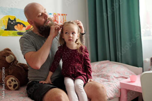 Photography Young bearded man sitting on bed of his adorable blond daughter in smart dress a