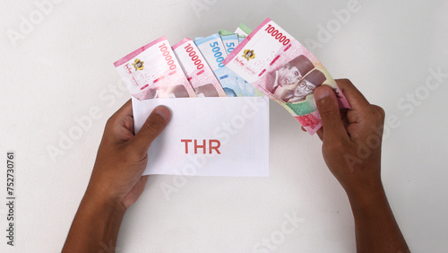 Hand holding a THR envelope filled with Indonesian Rupiah banknotes. THR or Tunjangan Hari Raya is a holiday allowance or bonus traditionally given to employees and those in need near during Ramadan photo