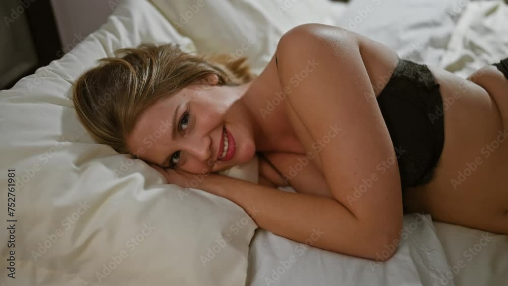 A smiling young adult woman with short blonde hair lying in bed, portraying a relaxed and intimate bedroom scene. A smiling young adult woman with short blonde hair lying in bed, portraying a relaxed and intimate bedroom scene.