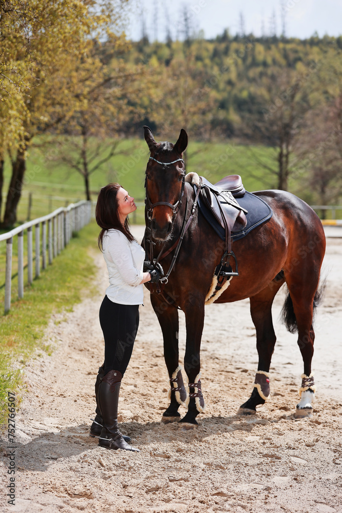 Young Frtau rider with brown long hair in portrait with her horse on the riding arena. Young Frtau rider with brown long hair in portrait with her horse on the riding arena.
