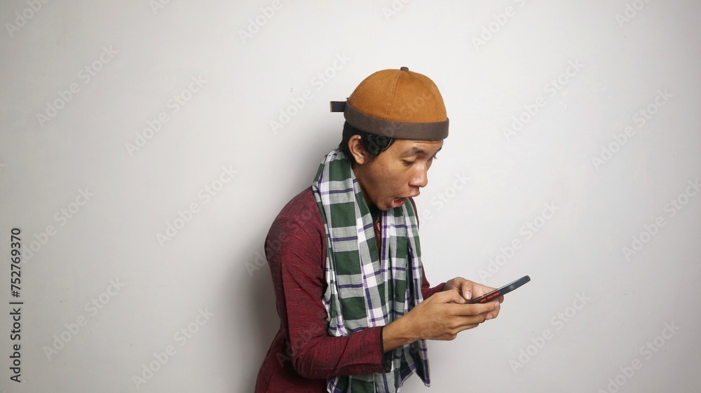 shocked Asian Muslim man playing, typing on smartphone shocked Asian Muslim man playing, typing on smartphone