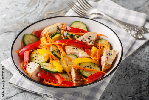 Healthy food Chicken salad with fresh cucumbers, bell peppers, carrots and sesame seeds close-up in a bowl on the table. Horizontal