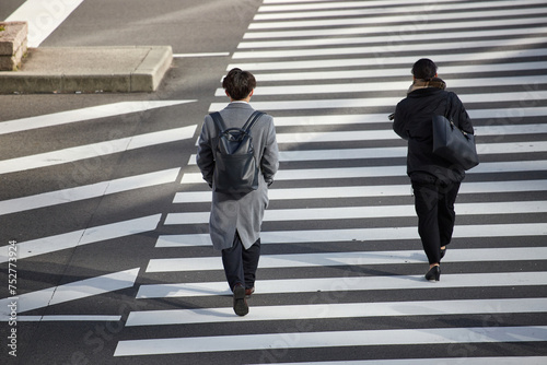 冬の朝の通勤時間の都市の交差点の横断歩道を渡る男女会社員の姿