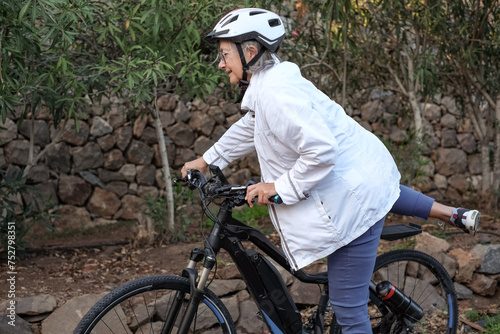 Smiling senior woman with helmet in outdoors activity with electric bicycle. Elderly lady in healthy activity with bike in the park