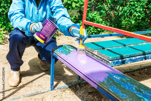 A woman paints a bench with alkyd enamel in a playground at a kindergarten photo