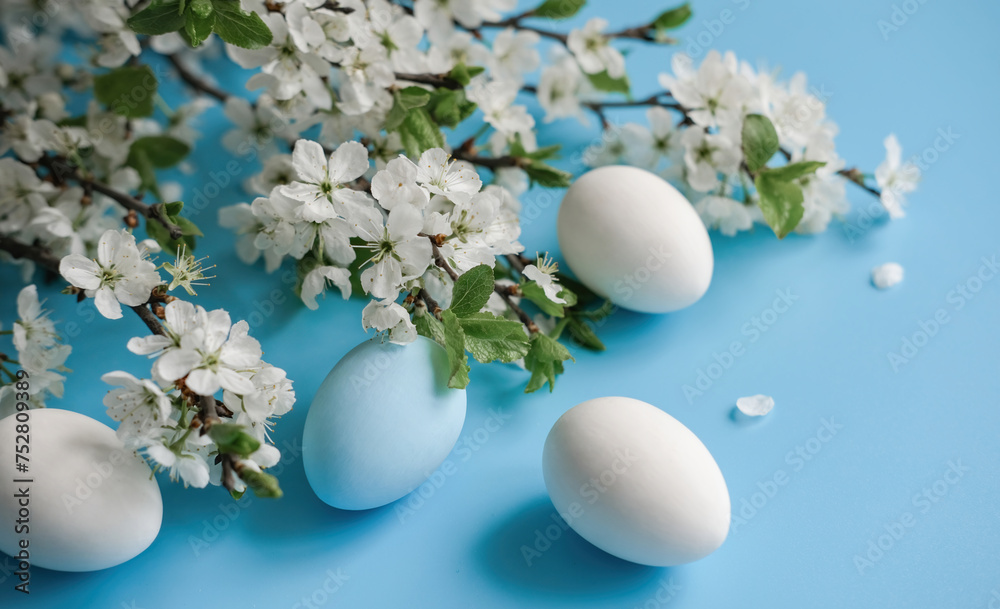 White and blue eggs amidst cherry blossoms on a vibrant blue backdrop signifying Easter and spring
