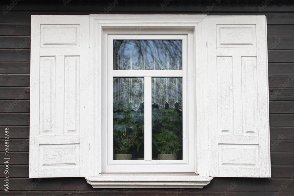 Fototapeta premium Wooden rustic window in cottage house. Abandoned forsaken wooden home. Rusty architecture. Podlasie region in Poland vintage wall. Peeling paint decorative exterior shutter. Dark wood home wall facade