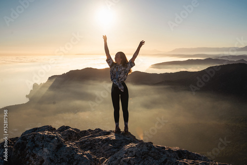 Happy girl on mountain peak with raised arms looking at beautiful mountain valley at sunset in summer. Landscape with sporty young woman. Travel and tourism. Hiking. Travel concept  © Соня Монштейн