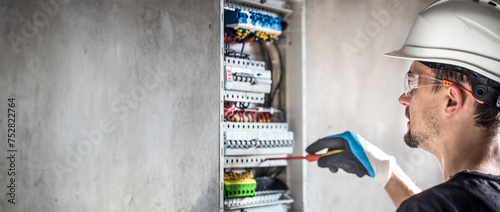 Male electrician working in switchboard with electrical connection cable. photo