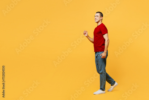 Full body side profile view smiling happy cheerful young middle eastern man he wear red t-shirt casual clothes walk go isolated on plain yellow orange background studio portrait. Lifestyle concept.