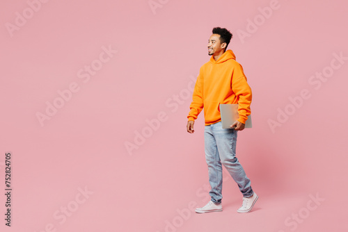 Full body young IT man of African American ethnicity he wear yellow hoody casual clothes hold use work on laptop pc computer isolated on plain pastel light pink background studio. Lifestyle concept.