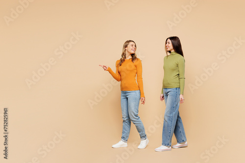 Full body young friend two women they wear orange green shirt casual clothes together walk go point index finger aside on area isolated on plain pastel light beige background studio Lifestyle concept