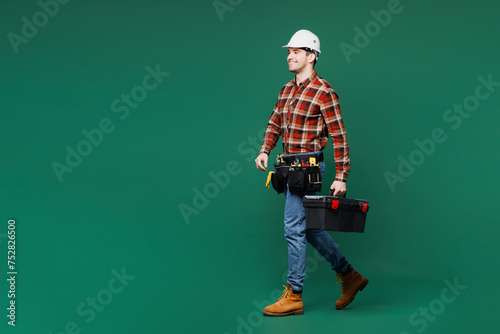 Full body side view young employee laborer man wear red shirt hardhat hat work hold toolbox isolated on plain green background Instrument accessories for renovation apartment room Repair home concept © ViDi Studio