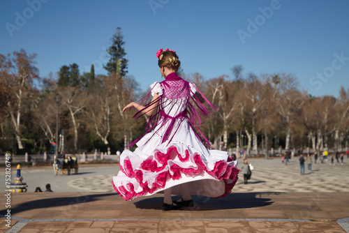 Girl dancing flamenco, twirling to show off her costume, in typical flamenco dress on a bridge in a beautiful square in Seville. Dance concept, flamenco, typical Spanish, Seville, Spain.