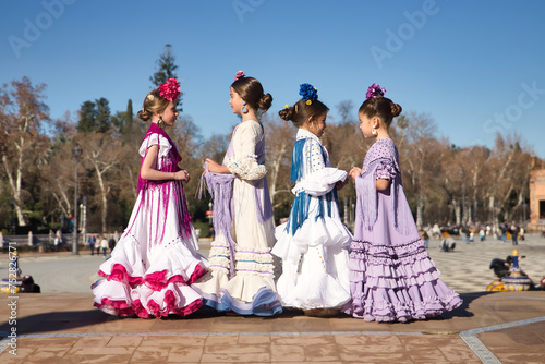 Four girls dancing flamenco, talking to each other, in typical flamenco costumes on a bridge in a beautiful square in Seville. Dance concept, flamenco, typical Spanish, Seville, Spain. © Manuel