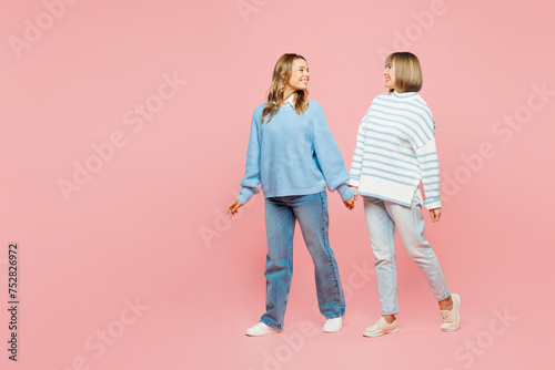 Full body happy cheerful elder parent mom with young adult daughter two women together wear blue casual clothes walk go look to each other isolated on plain pastel pink background. Family day concept.