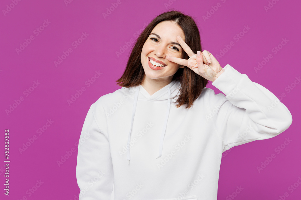 Young smiling happy Caucasian woman she wear light hoody casual clothes show cover eye face with victory sign look camera isolated on plain purple color background studio portrait. Lifestyle concept.