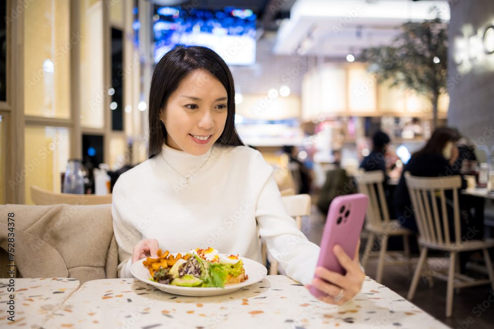 Woman enjoy her salad and take selfie on mobile phone in restaurant