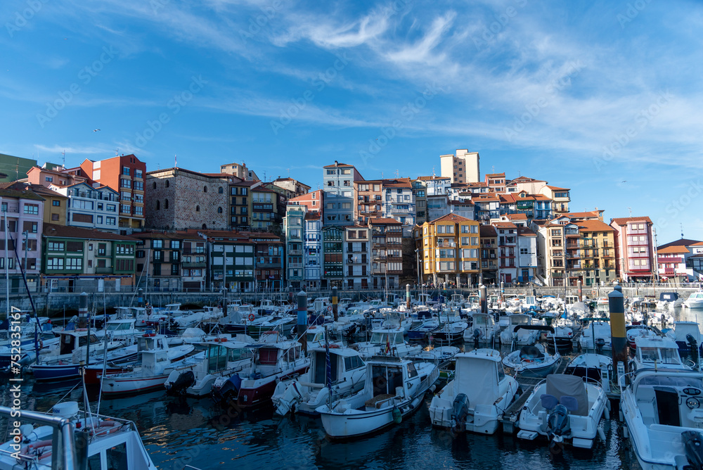 Panoramic view of the touristic Basque coastal town of Bermeo, in front of a small harbour full of boats and their colourful facades on a sunny day.