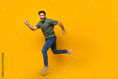 Full body photo of attractive young man running fast have fun dressed stylish khaki clothes isolated on yellow color background