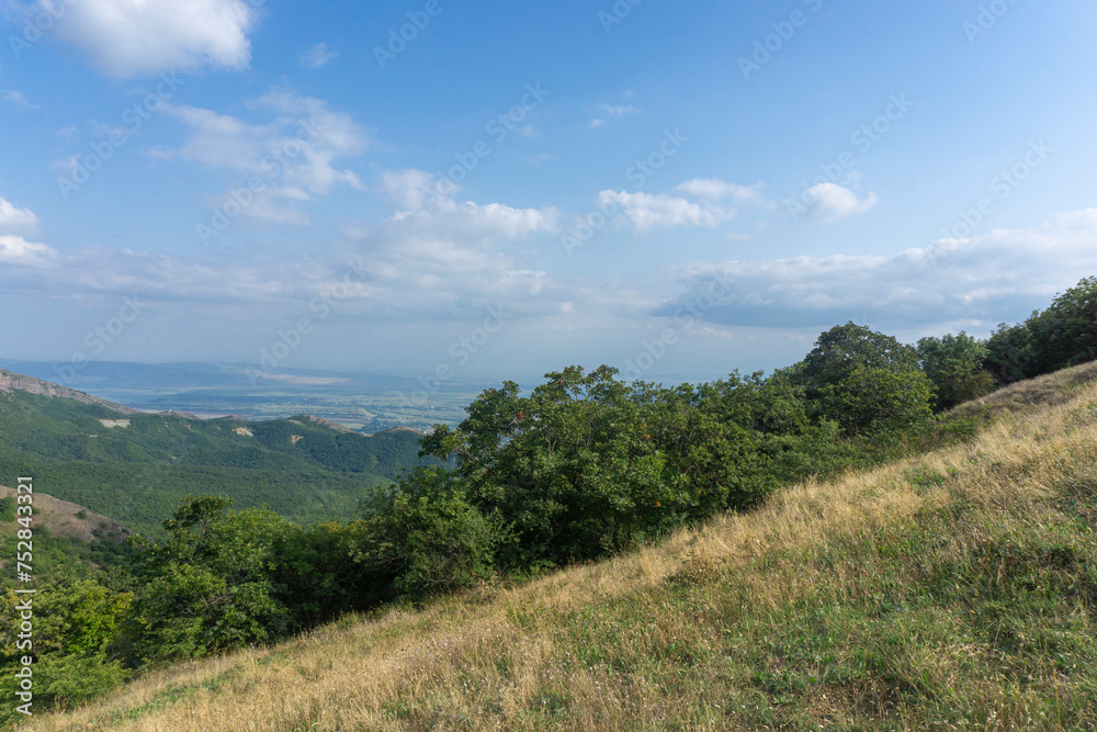 Landscape of rocks and mountains. Bright blue sky and clouds. Green grass on the foreground.  View of nearby mountains and villages. Georgia.