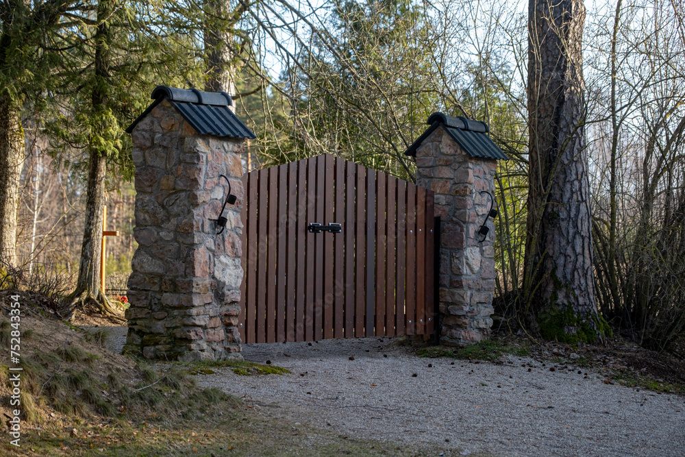 brown wooden cemetery gate with stone columns. Latvian forest graveyards. brown wooden cemetery gate with stone columns. Latvian forest graveyards.