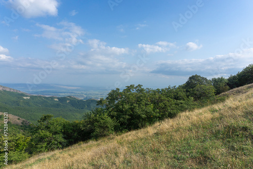 Landscape of rocks and mountains. Bright blue sky and clouds. Green grass on the foreground. View of nearby mountains and villages. Georgia.