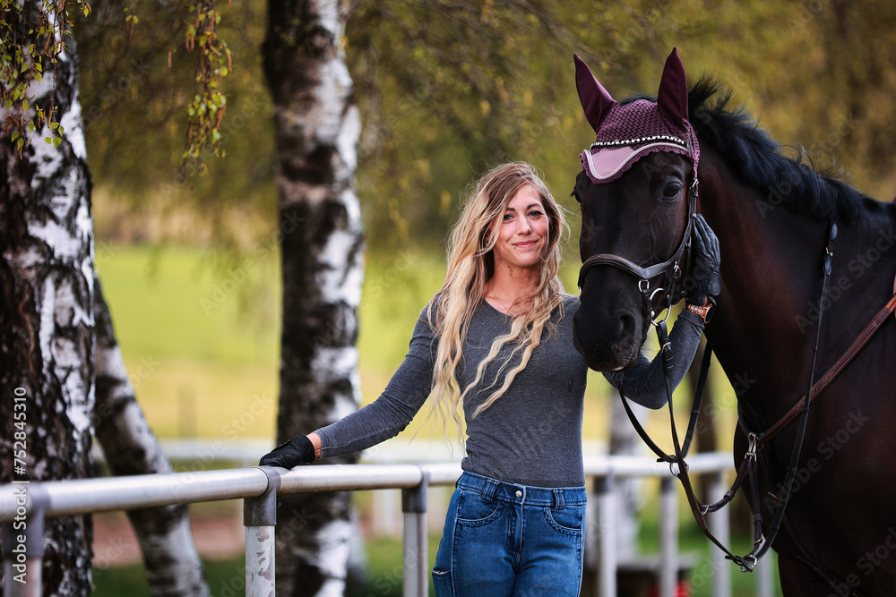 Obraz premium Young woman with long hair and blonde streaks, stands portraits with her horse.
